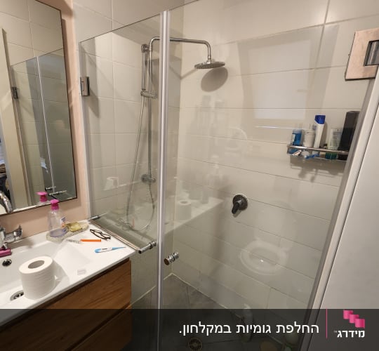מקלחון זכוכית פינתי מותקן בחדר רחצה לצד ארון כיור